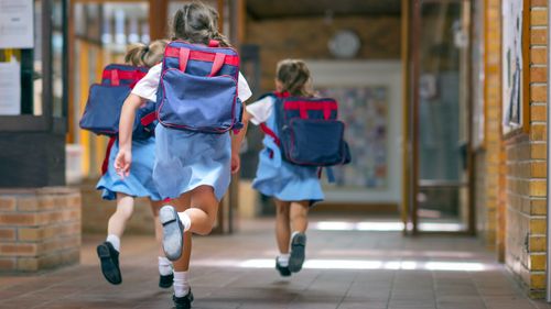 Rear view of excited students running towards entrance. Girls are carrying backpacks while leaving from school. Happy friends are wearing school uniforms.
