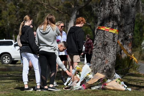 Grieving community members place flowers at the base of a tree where 5 people were killed in a motor vehicle accident last night on East Parade in Buxton, NSW. 7th September, 2022. Photo: Kate Geraghty