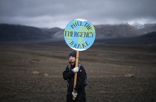 A girl holds a sign that reads 'pull the emergency brake' as she attends a ceremony in the area which once was the Okjokull glacier, in Iceland