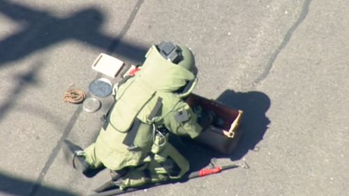 An officer wearing a bomb disposal suit examines the device. (9NEWS)