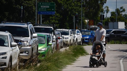 Photographs show scenes from todays Covid-19 drive through testing clinic on Mulgoa Road, Penrith. Waiting times of up to 2 hours forced some like Western suburbs resident Michael to walk his baby in a stroller, talking to his wife,  alongside her in queue  in a silver 4WD. Photographs taken Thursday 30th December 2021. Photographs by Dean Sewell.