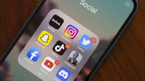 Assorted popular social media apps - BeReal, Instagram, Twitter, Snapchat, TikTok, Clubhouse, Facebook, YouTube, and Discord - are seen on an iPhone. 