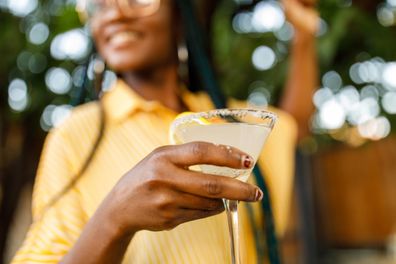 Low angle view of cheerful young woman holding and enjoying a martini glass with margarita cocktail during a relaxing summer garden party. Part of a series.