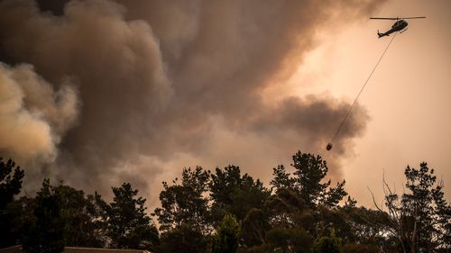 Helicopters dump water on bushfires as they approach homes located on the outskirts of the town of Bargo on December 21, 2019