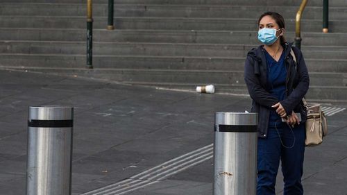 A woman wearing a face mask is seen on a very quiet Flinders Street in Melbourne. 