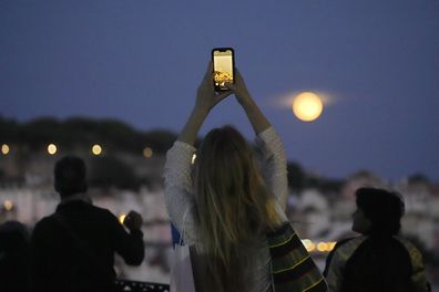 A woman takes pictures of a supermoon rising above Lisbon, Wednesday, Aug. 30, 2023. 
