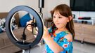 little beauty blogger filming videos at home and dancing to camera set on ring light, young blogger concept, copy space