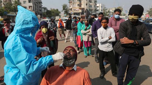 A health worker takes a swab sample of a man to test for the coronavirus as others wait to get tested in Ahmedabad, India.