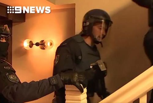 A police officer takes an axe to break down a door during the Kings Cross raids today.