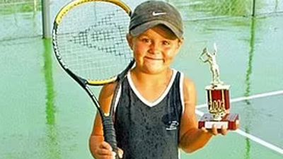 A young Ash Barty holding a tennis racquet and a trophy.