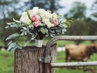 Wedding flowers sitting on fence gate post in rural scene.