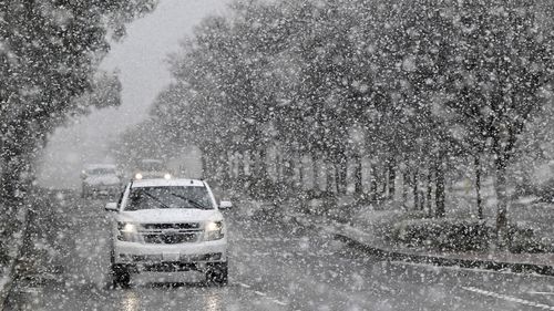 A vehicle makes its way across Wilson Avenue in Rancho Cucamonga, California, as snow begins to blanket the area.