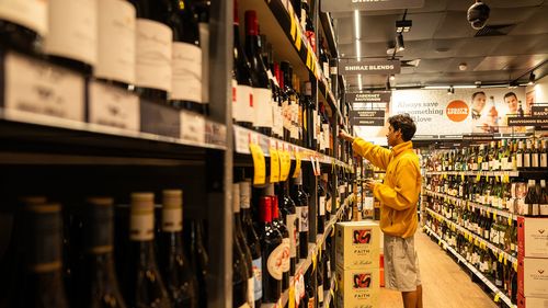Someone selects a bottle of wine from a shelf in a bottle shop