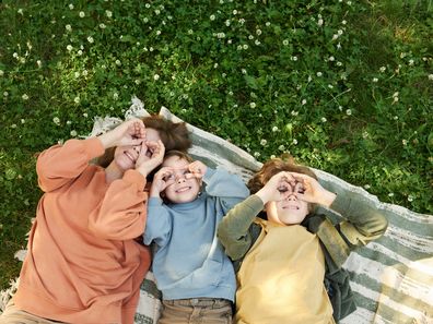Mum relaxes in a park on picnic blanket beside two boys.
