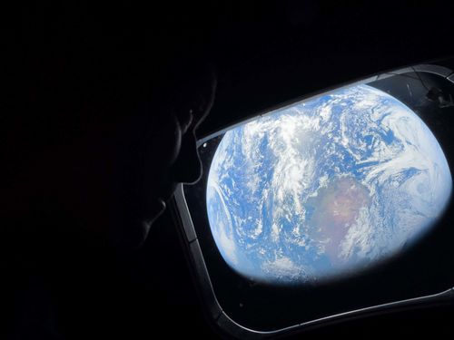 Commander Reid Wiseman looks at the Earth from a window aboard the Orion spacecraft Integrity.