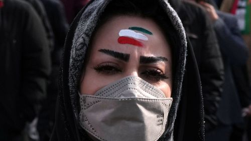 A woman with forehead painted with the Iranian flag's colors takes part in the annual rally commemorating Iran's 1979 Islamic Revolution