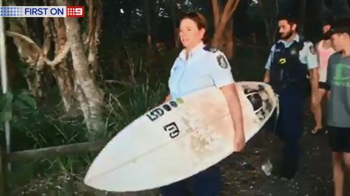 A NSW police officer carries a surfboard from the beach. (9NEWS)