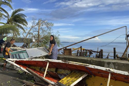 Residents carry what's left of their belongings as they walk past a damaged boat due to Typhoon Rai in Surigao city, Surigao del Norte, central Philippines on Friday Dec. 17, 2021 