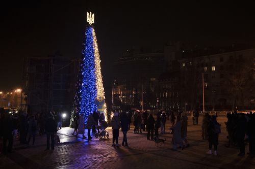 Люди собираются вокруг рождественской елки, украшенной цветами украинского государственного флага, на Софийской площади в Киеве, Украина, пятница, 23 декабря 2022 года.  