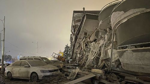 Damaged vehicles sit parked in front of a collapsed building following an earthquake in Diyarbakir, southeastern Turkey, early Monday, Feb. 6, 2023.