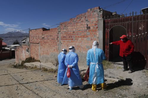 Healthcare workers dressed in full protective gear speak with a woman during a house-to-house coronavirus testing drive in Villa El Rosal, on the outskirts of La Paz, Bolivia