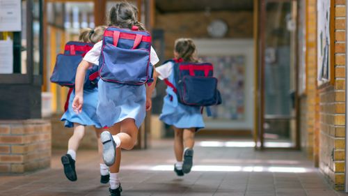 Rear view of excited students running towards entrance. Girls are carrying backpacks while leaving from school. Happy friends are wearing school uniforms.