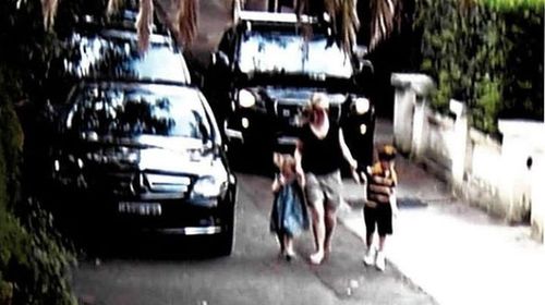 A car drives down a footpath behind some pedestrians.