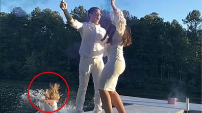 A couple celebrating their gender reveal while a woman jumps into the lake behind them.