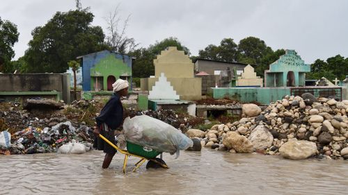 A woman pushes a wheelbarrow while walking in a partially flooded street, in the Haitian capital, Port-au-Prince. (AFP)