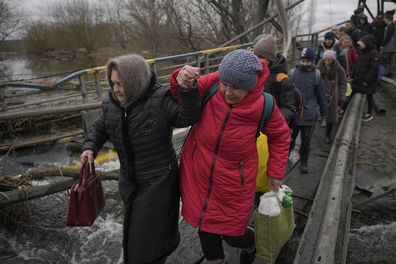 Women hold hands while crossing the Irpin river on an improvised path under a bridge that was destroyed by a Russian airstrike, while assisting people fleeing the town of Irpin, Ukraine, Saturday, March 5, 2022. What looked like a breakthrough cease-fire to evacuate residents from two cities in Ukraine quickly fell apart Saturday as Ukrainian officials said shelling had halted the work to remove civilians hours after Russia announced the deal. (AP Photo/Vadim Ghirda)