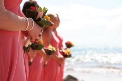 Bridesmaids hold colorful tropical bouquets at a wedding ceremony on a island beach.