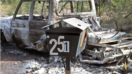 The burnt-out remains of a police vehicle and a fake security camera on a mailbox next to the front gate of the Train family property at Wieambilla in Queensland.