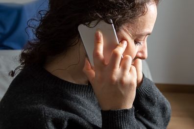 Close-up of Serious woman attending a phone call sitting on a bed in the bedroom