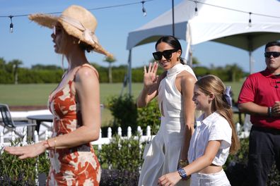 Meghan Markle, Duchess of Sussex, waves to the press as she walks with Delfina Blaquier, left, and Alba Figueras at the 2024 Royal Salute Polo Challenge to Benefit Sentebale, Friday, April 12, 2024, in Wellington, Florida