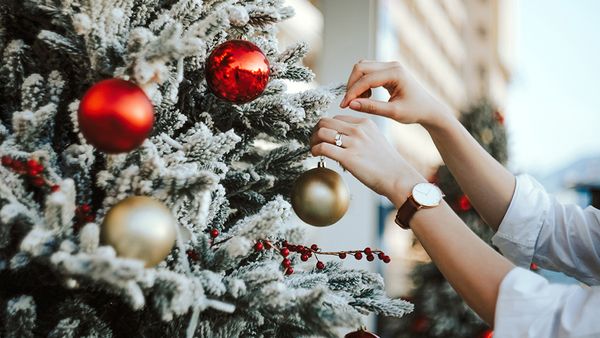 Cropped hand of woman decorating and hanging baubles on Christmas tree