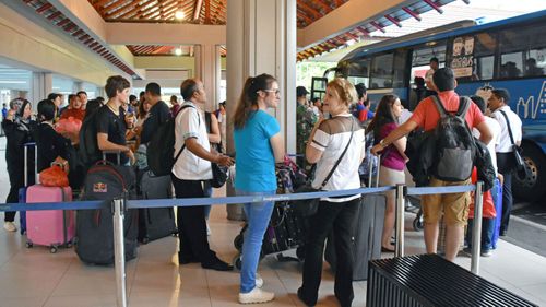 Tourists wait for a bus at Bali airport. (Image: AAP)