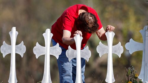 Maria Durand, a Bible study teachers aid at First Baptist Church of Sutherland Springs, leans over while hanging onto two of the 26 crosses representing the victims in Sutherland Springs, Texas. (AAP)