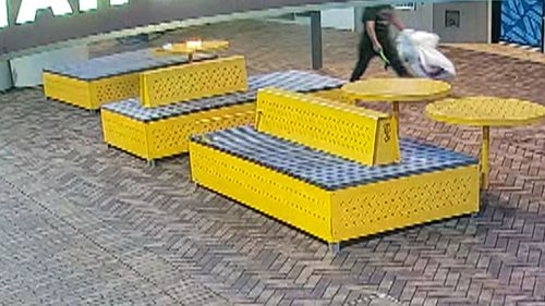 CCTV shows a man yelling and walking through the shopping strip with an axe while carrying shopping bags.
