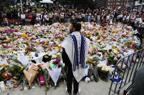 Rabbi Yossi Friedman speaks to people gathering at a flower memorial by the Bondi Pavilion at Bondi Beach.