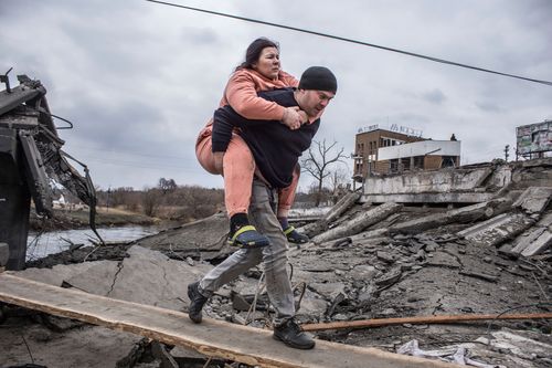 A man carries a woman as they cross an improvised path while fleeing the town of Irpin, Ukraine.