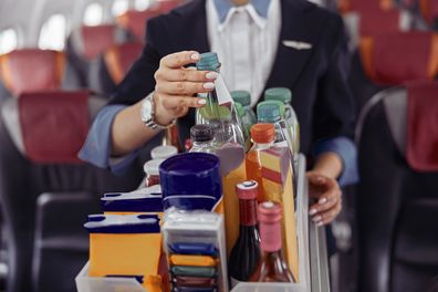 Stewardess take water bottle from trolley cart in passenger cabin of airplane jet. Modern plane interior. Cropped image of woman wear uniform. Civil commercial aviation. Air travel concept