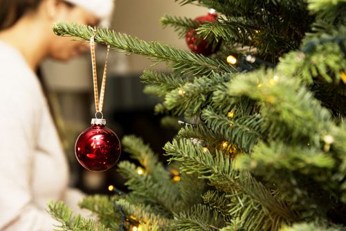 Defocused woman working on hanging ornaments on a tree, with a close up of a tree ornament hanging off the side