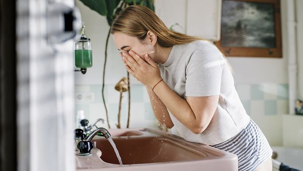 Woman bending over bathroom sink washing her face.