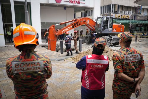 Fire and Rescue department checking on after receiving reports that a woman has fallen into the sinkhole after a section of the sidewalk caved in Kuala Lumpur, Friday, Aug. 23, 2024. 