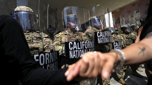 Protesters clasp hands in front of a line of California National Guard, Monday, June 9, 2025, at a Federal Building in downtown Los Angeles. (AP Photo Jae Hong)
