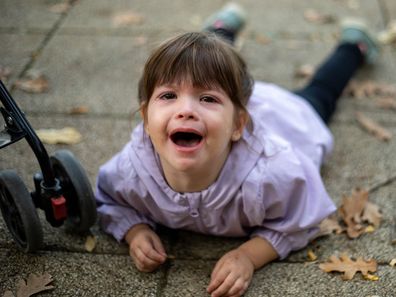 The girl is tired. She doesn't want to walk and she doesn't want to ride in a stroller, so she decided to lie down and cry.