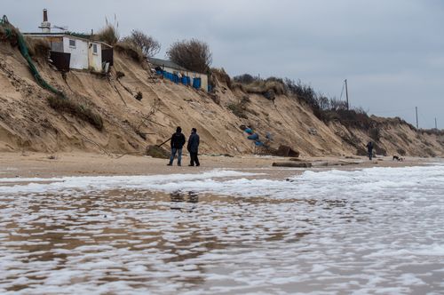 Two men stand on Hemsby beach in front of houses that have been evacuated after high winds and waves eroded the dunes on which they sit on March 18, 2018 in Norfolk, England. Ten sea front properties have been evacuated after severe weather rapidly eroded the cliff edges in the village of Hemsby. (Photo by Chris J Ratcliffe/Getty Images)
