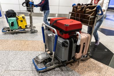 Traveler pushes trolley with suitcases and bags in airport terminal after arrival