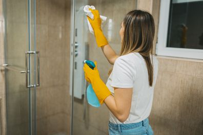A woman polishing a front side of the shower. Clean and shiny glass.