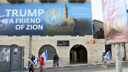 People walk past signs in Jerusalem, that show support for US President Donald Trump's decision to move the country's Embassy to the city.